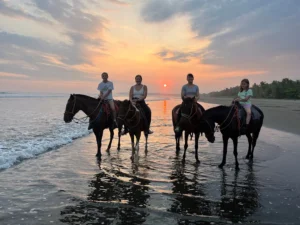 A family of four horseback riding on the beach at sunset in Jaco, Costa Rica