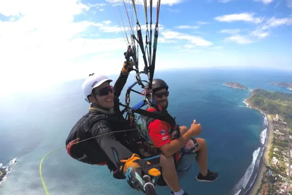Two boys flying in a tandem paraglider over Jacó beach in Costa Rica